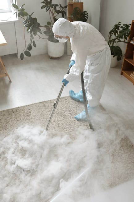 A woman with curly hair, dressed in a beige jacket, blue jeans, and white shoes, is engaged in deep surface cleaning using a vacuum cleaner with a yellow body and black hose attachment. She is vacuumi